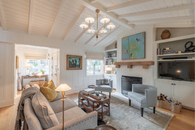 Spacious main living room with a brick fireplace, custom built-ins, and beamed ceilings in Carmel cottage.
